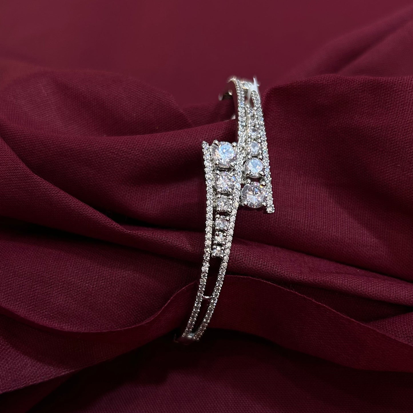 A silver-toned double-band ring set with clear pavé stones, displayed on draped burgundy fabric.