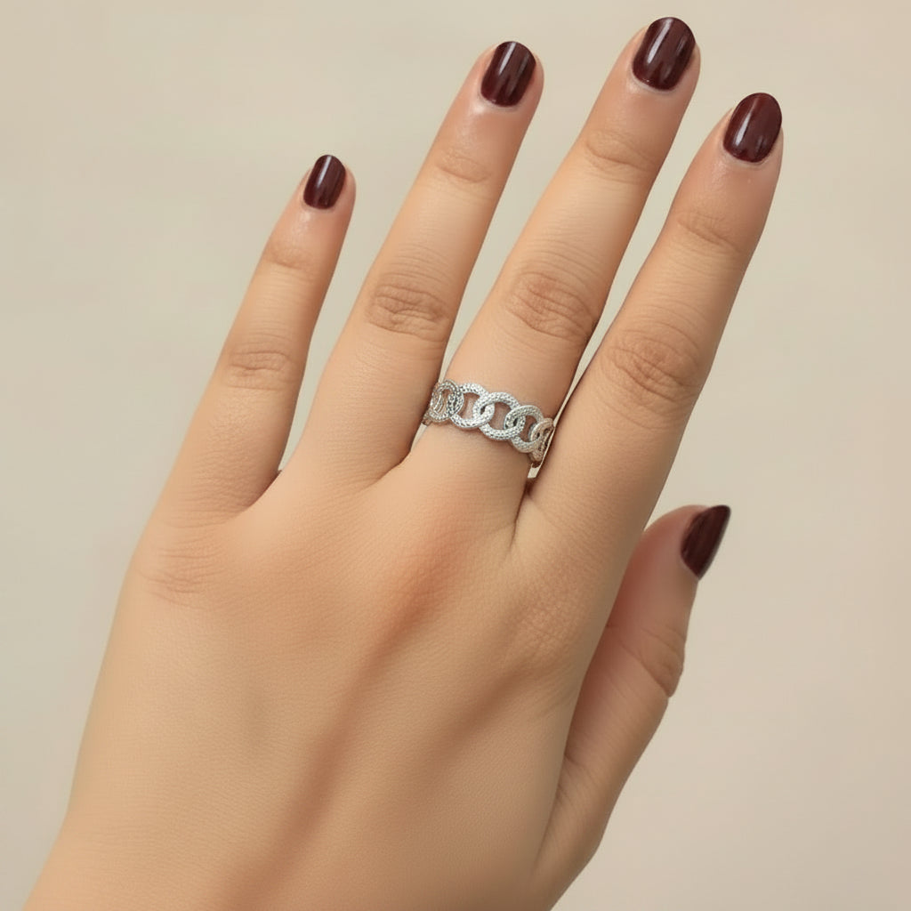 A close-up of a hand wearing two silver rings, one with a textured geometric pattern and the other with a polished interlocking chain design, resting on a black leather surface.