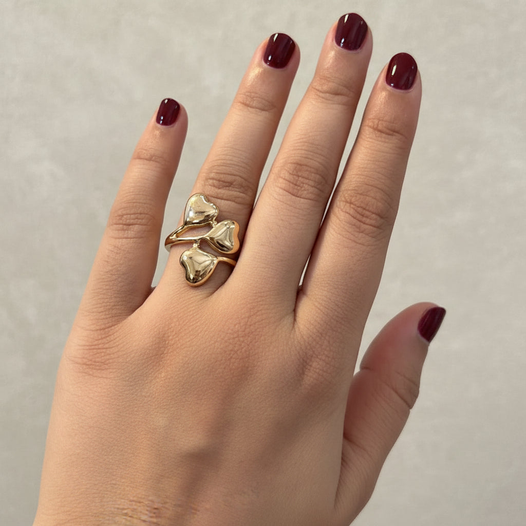 A close-up of a hand wearing a chunky gold ring with a textured, organic knot-like design and clear stones, resting on a black leather surface.