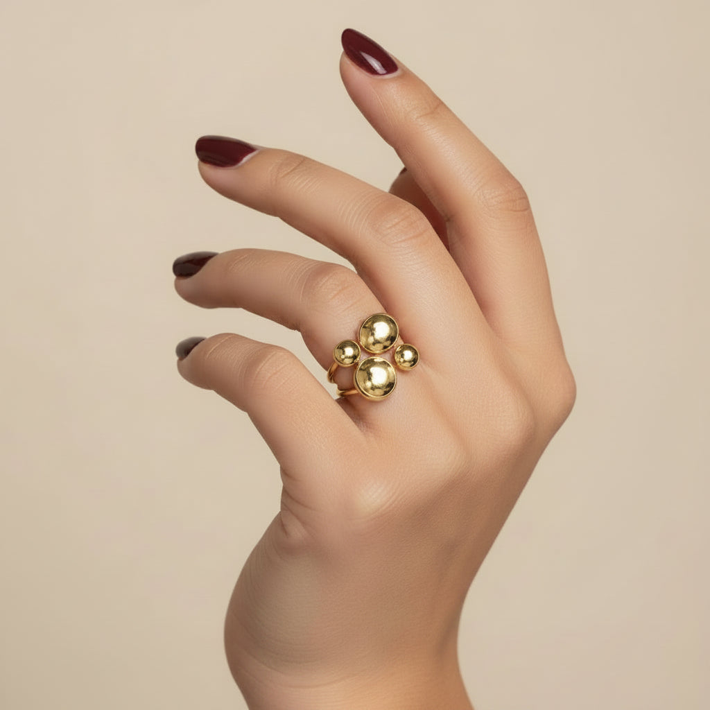 A close-up of a hand wearing a gold ring with four round clear stones, resting on a dark textured surface.