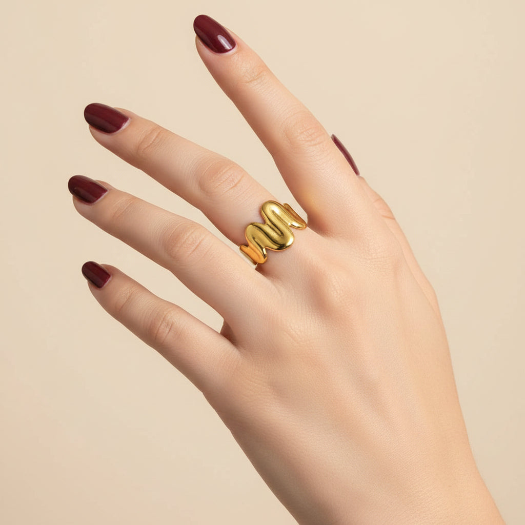 A gold snake-shaped ring worn on a person's hand, resting on a black textured surface.