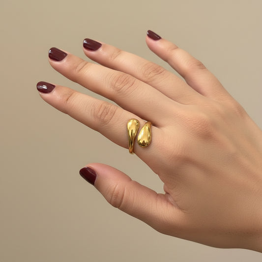 A gold ring with a textured, snake-like coiled design worn on a person's ring finger, shown against a dark black leather background.