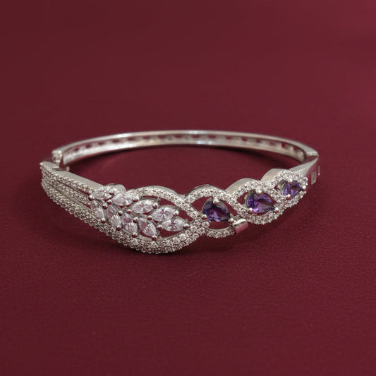 A silver-toned hinged bangle bracelet featuring pavé-set clear stones and three oval purple amethyst gemstones, displayed on a dark red background.