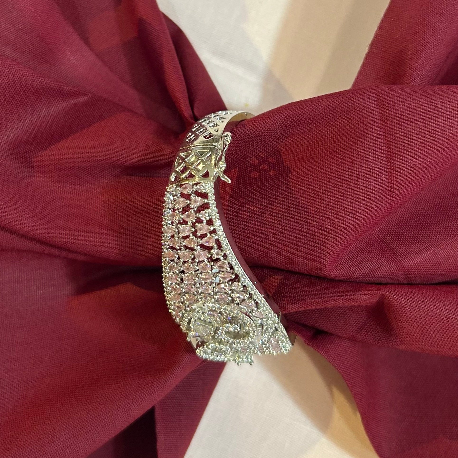 A close-up of a silver-toned, diamond-embellished ring-shaped decorative pin or brooch fastened to a draped burgundy fabric against a light cream background.