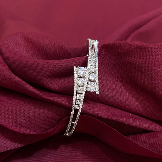 A silver-toned bangle bracelet with pavé-set clear stones, displayed on draped burgundy fabric.