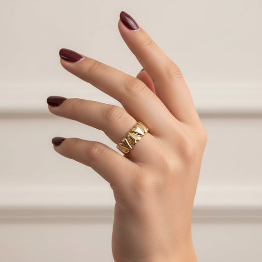 A close-up of a hand wearing a gold ring with three small white stones, resting on a dark textured surface.