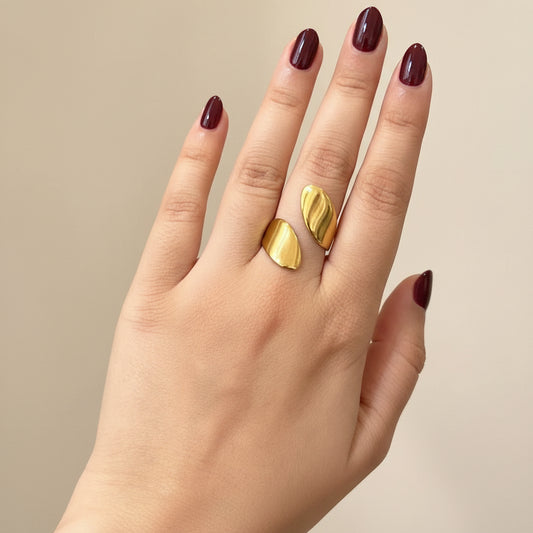 A close-up of a person's hand resting on a black textured surface, wearing two small gold crescent-shaped rings on the middle and ring fingers.