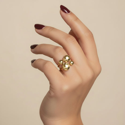 A close-up of a hand wearing a gold ring with four round clear stones, resting on a dark textured surface.