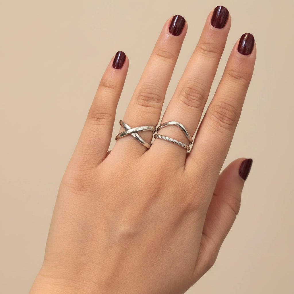 A close-up of a hand wearing two silver rings, resting on a black textured surface.