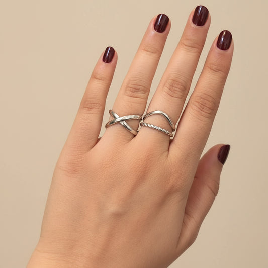 A close-up of a hand wearing two silver rings, resting on a black textured surface.