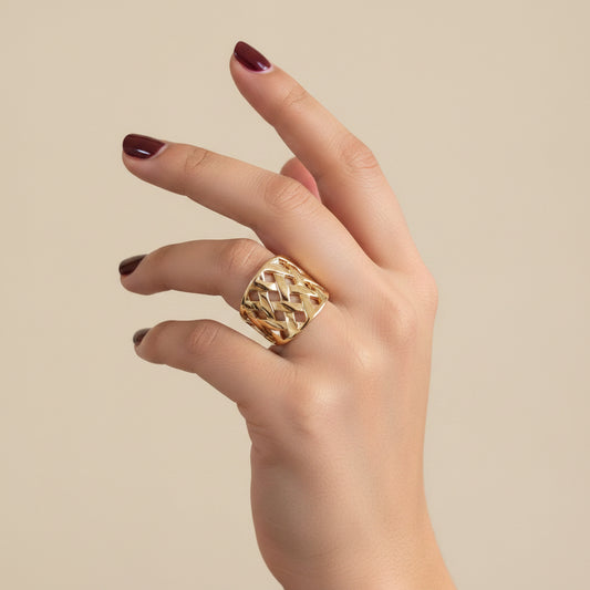 A gold ring with a textured, woven geometric pattern, worn on a person's ring finger against a black leather background.