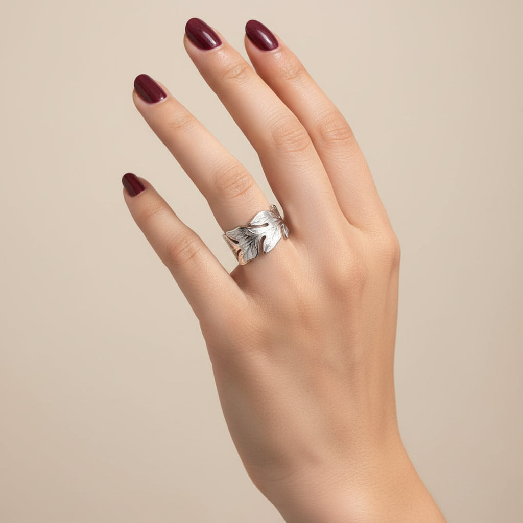 A silver-toned textured band ring worn on a person's ring finger, shown against a dark black leather surface.