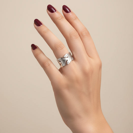 A silver-toned textured band ring worn on a person's ring finger, shown against a dark black leather surface.