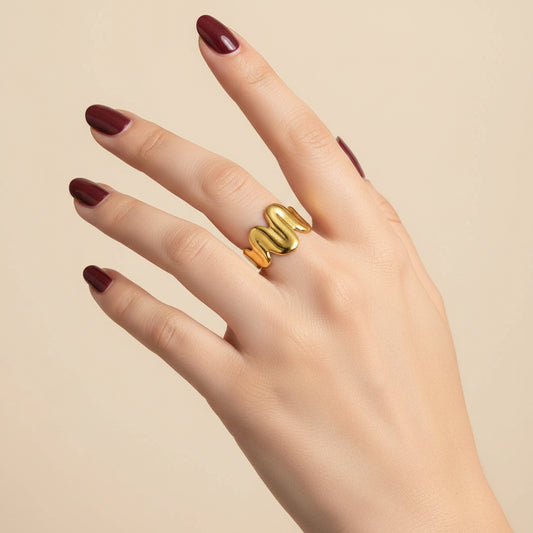 A gold snake-shaped ring worn on a person's hand, resting on a black textured surface.